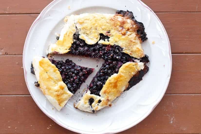 A rustic blueberry galette with two slices cut out, served on a white plate on a wooden table.