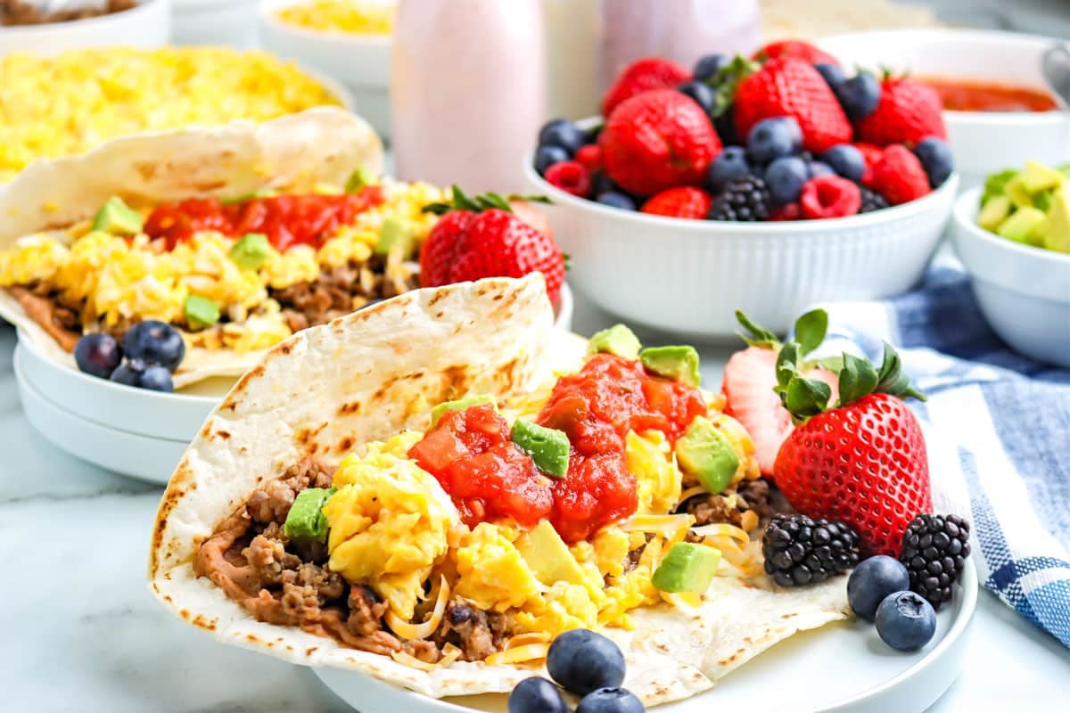 Breakfast tacos with scrambled eggs, avocado, salsa, and fruit served with mixed berries on the side.