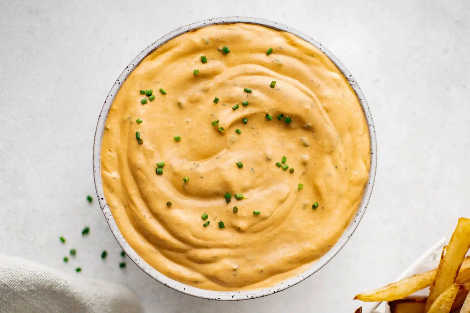 Bowl of creamy orange dipping sauce topped with chopped chives, with fries partially visible on the side.
