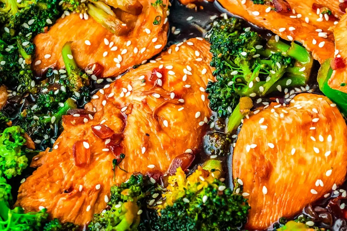 Chicken breast pieces with broccoli and sesame seeds cooked in a savory sauce, garnished with red chili flakes.