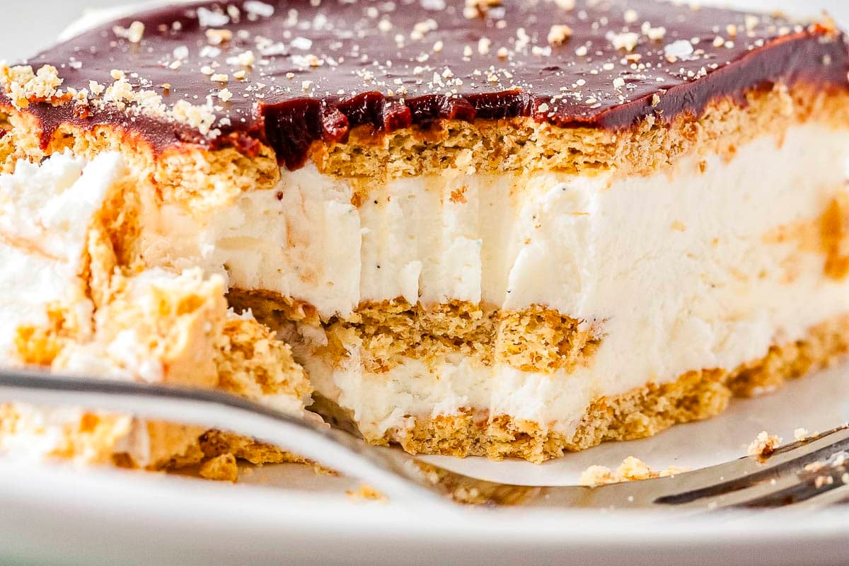 A close-up of a creamy layered dessert with graham crackers and chocolate topping on a plate with a fork.