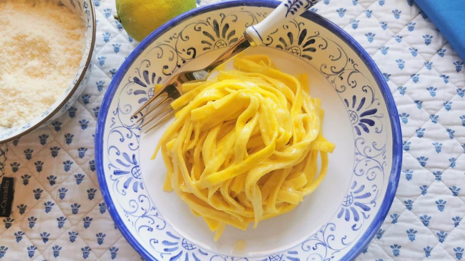 A plate of creamy yellow pasta with a fork on a blue and white patterned plate, seen from above.