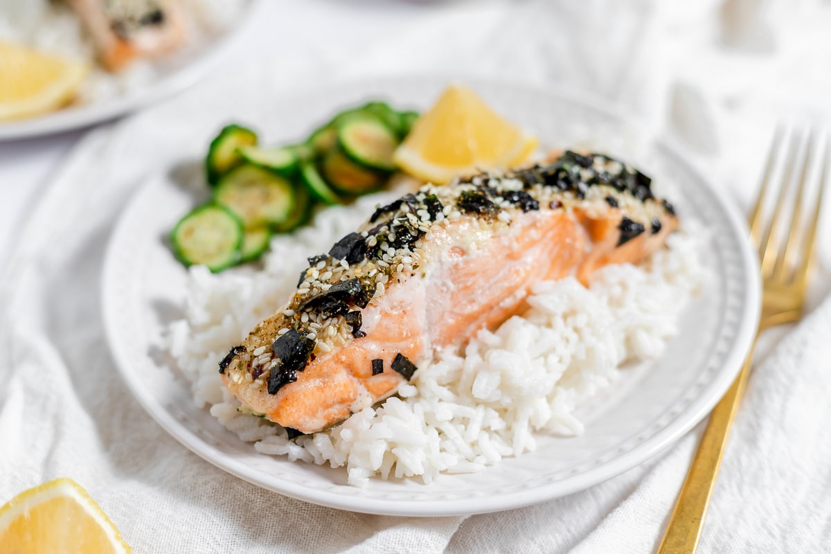 Baked salmon with seaweed, white rice, sliced zucchini, and lemon wedge on a white plate.