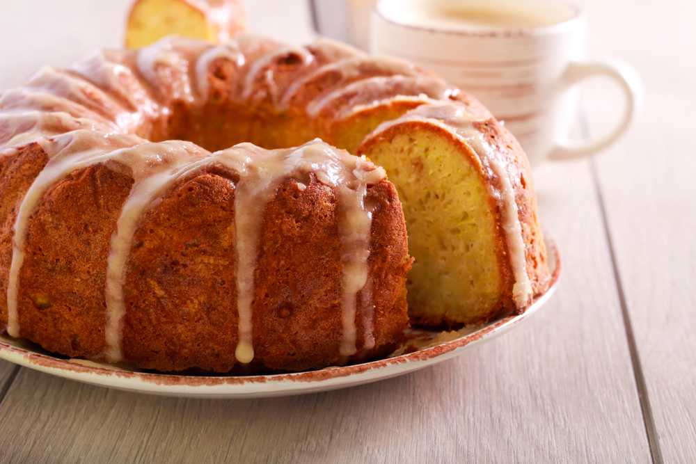 Glazed bundt cake with a slice cut out, served on a plate with a cup of coffee in the background.