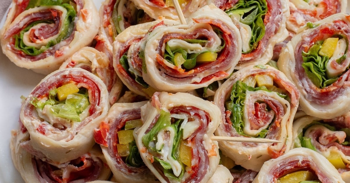 Close-up of tortilla pinwheels filled with deli meat, cheese, lettuce, and peppers, secured with toothpicks.