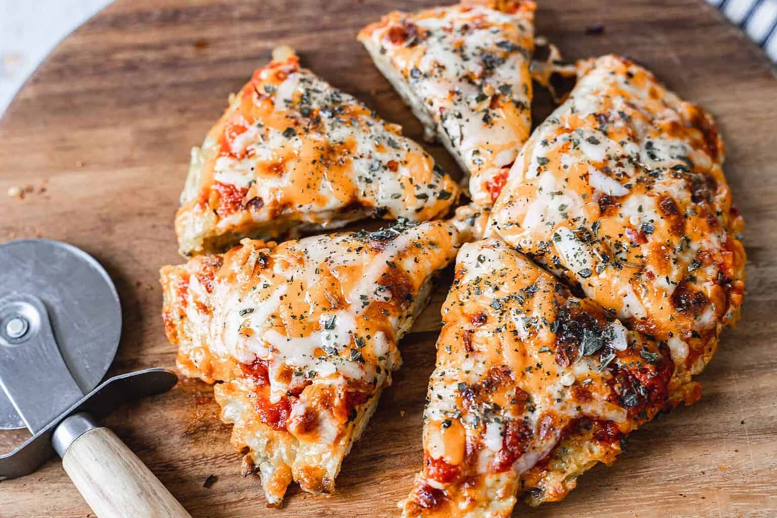 Six slices of cheesy pizza with herbs on a wooden board next to a pizza cutter.