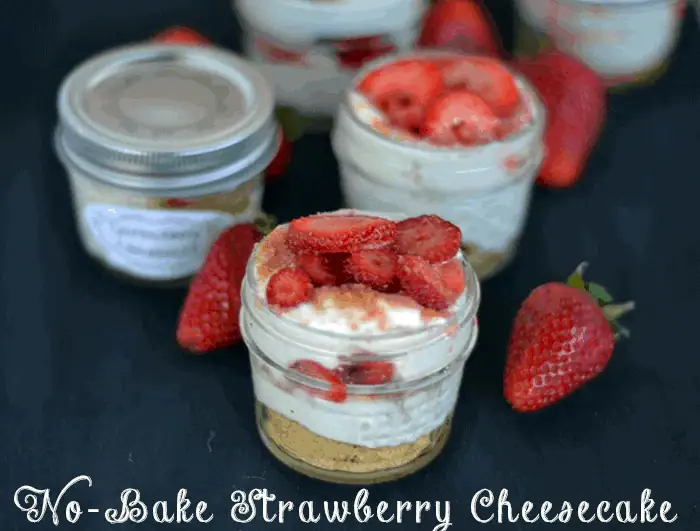 Small jars of no-bake strawberry cheesecake topped with fresh strawberries, surrounded by whole strawberries.