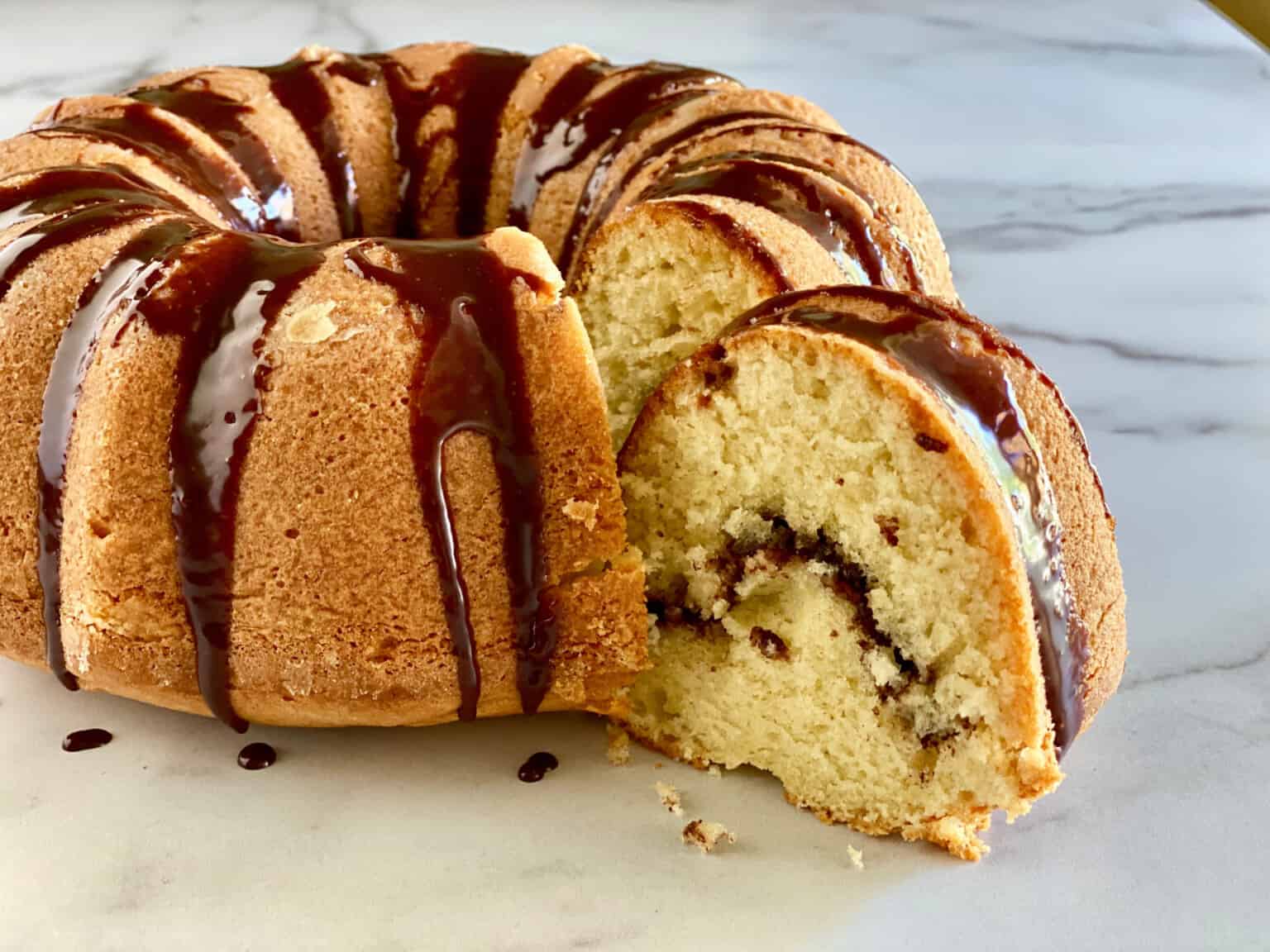 A sliced bundt cake with a chocolate drizzle on a marble surface.