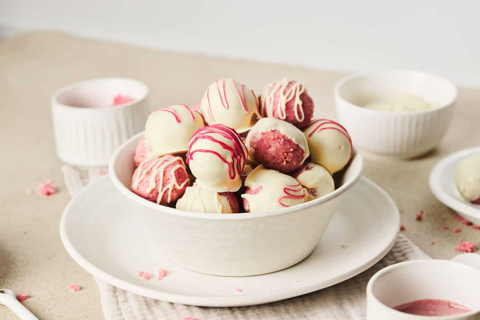 A bowl of white chocolate-covered truffles drizzled with pink icing, placed on a white plate.