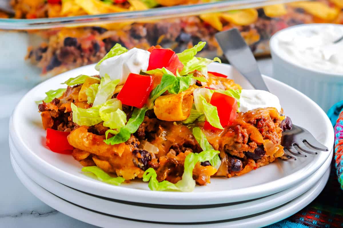 A plate of taco casserole topped with lettuce, tomato, and sour cream, with a fork on the side.