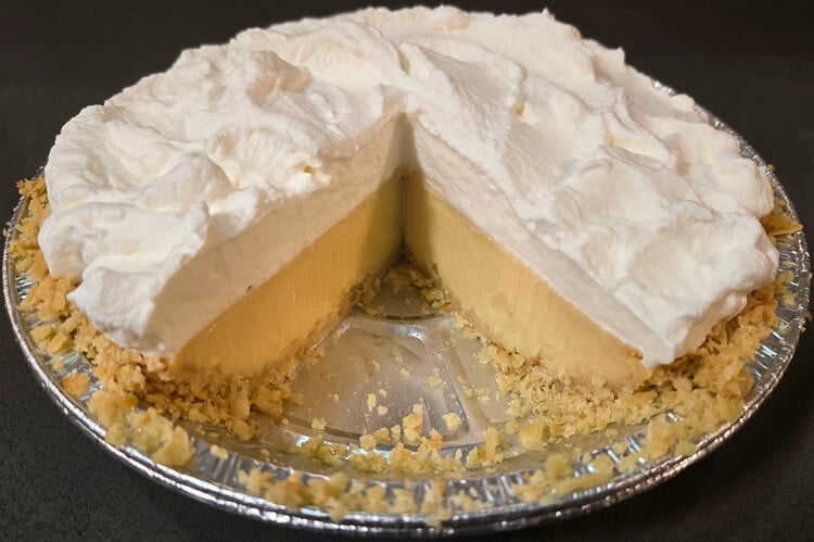 A cream pie with a slice missing, showing a thick custard filling and topped with whipped cream.