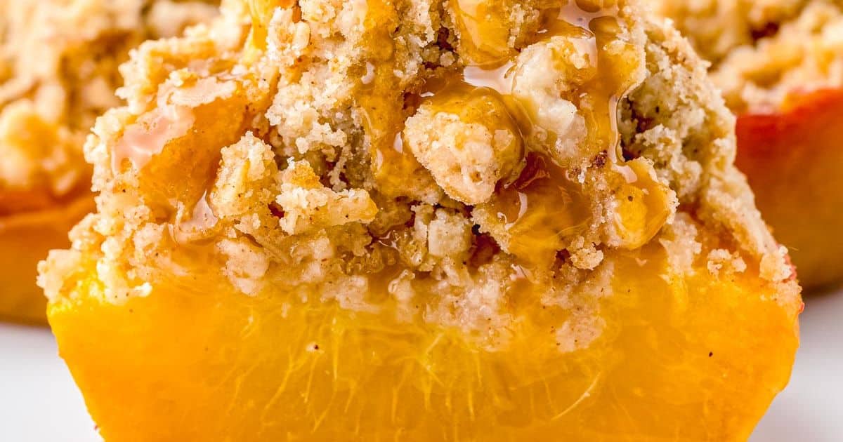Close-up of a baked peach half topped with crumbly streusel and drizzled with honey.