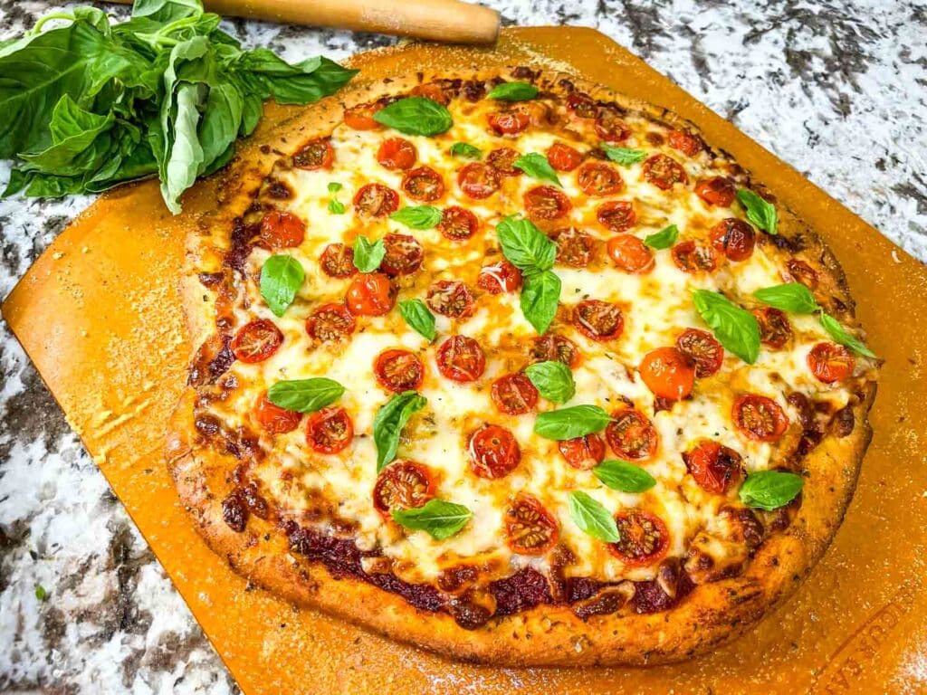 Homemade pizza topped with melted cheese, cherry tomatoes, and fresh basil leaves on a wooden board.