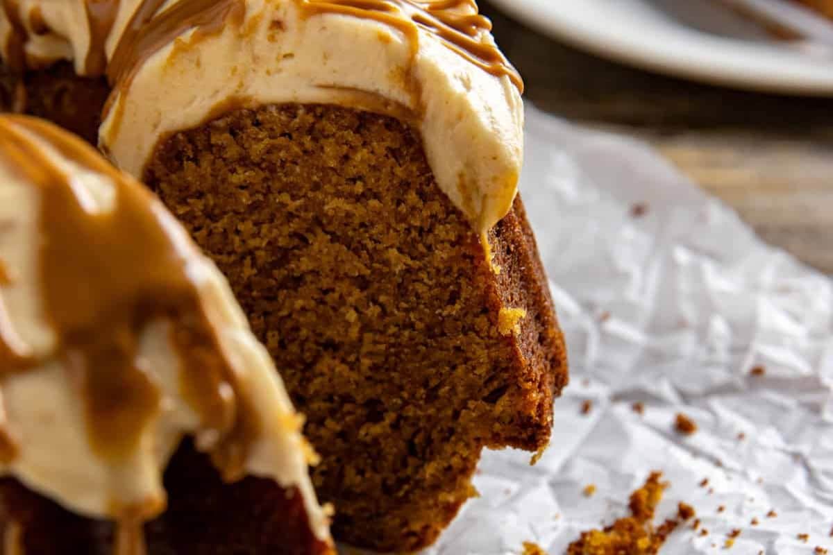 Close-up of a sliced bundt cake with creamy frosting and caramel drizzle on parchment paper.
