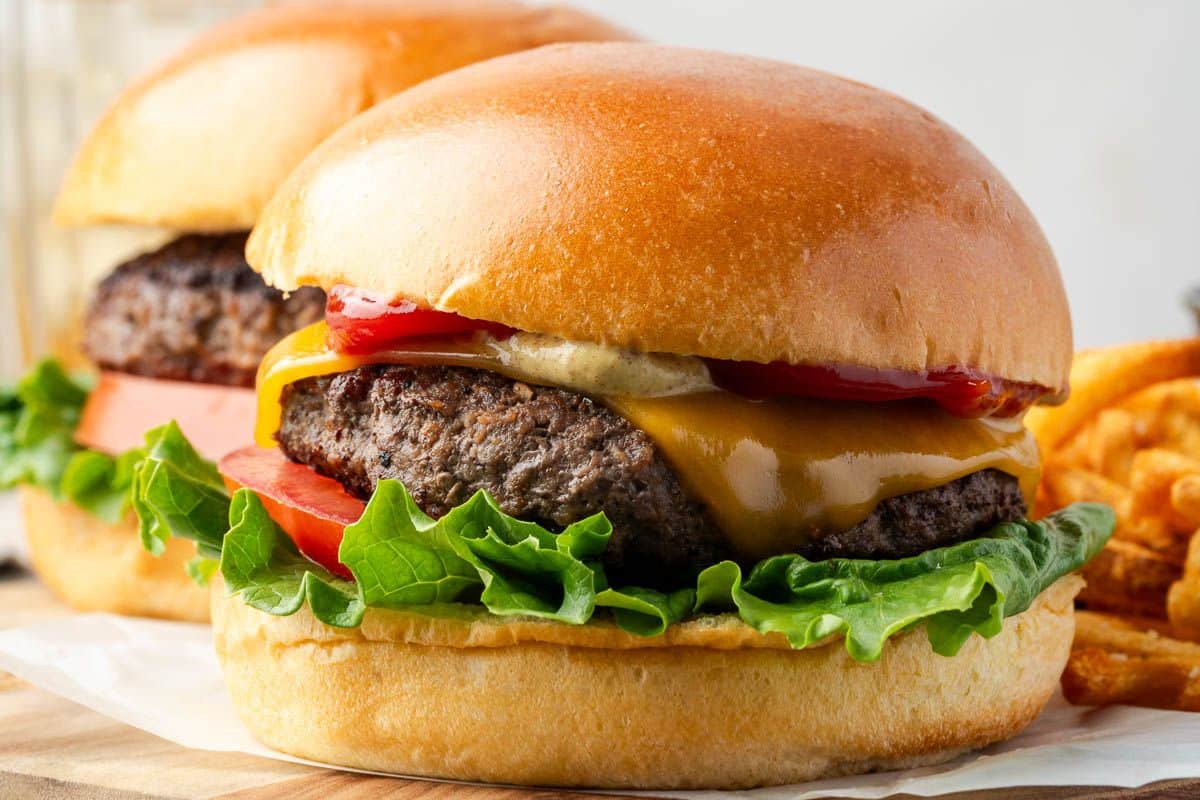 Close-up of a cheeseburger with lettuce, tomato, cheddar cheese, ketchup, and a brioche bun.