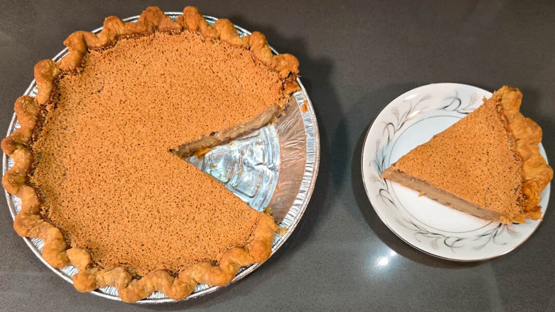 A whole pie with one slice missing, and the slice placed on a white patterned plate next to it.