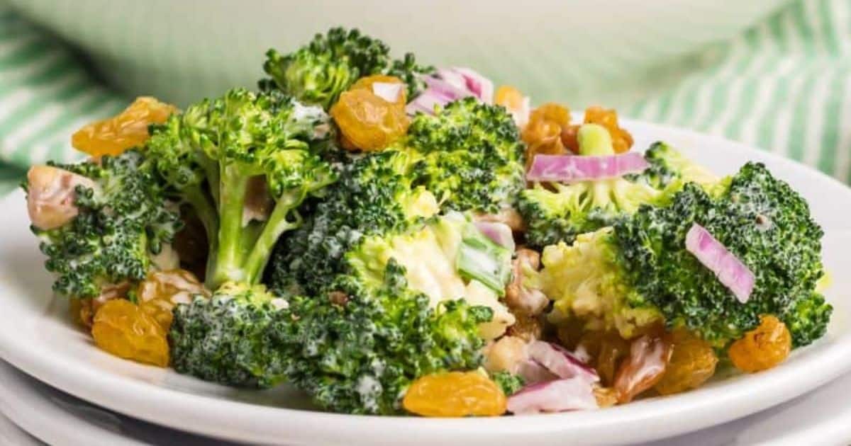 Broccoli salad with red onions, golden raisins, and creamy dressing served on a white plate.