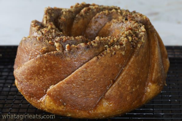 A freshly baked bundt cake topped with chopped nuts sits on a cooling rack.