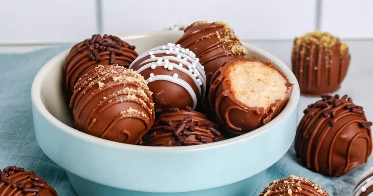 A bowl of assorted chocolate truffles, one with a bite taken out, on a blue cloth.