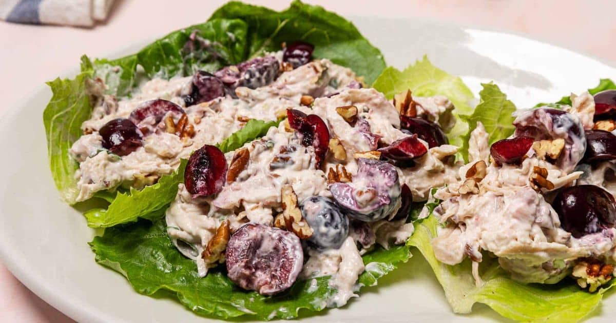 Chicken salad with grapes and pecans served on green lettuce leaves on a white plate.