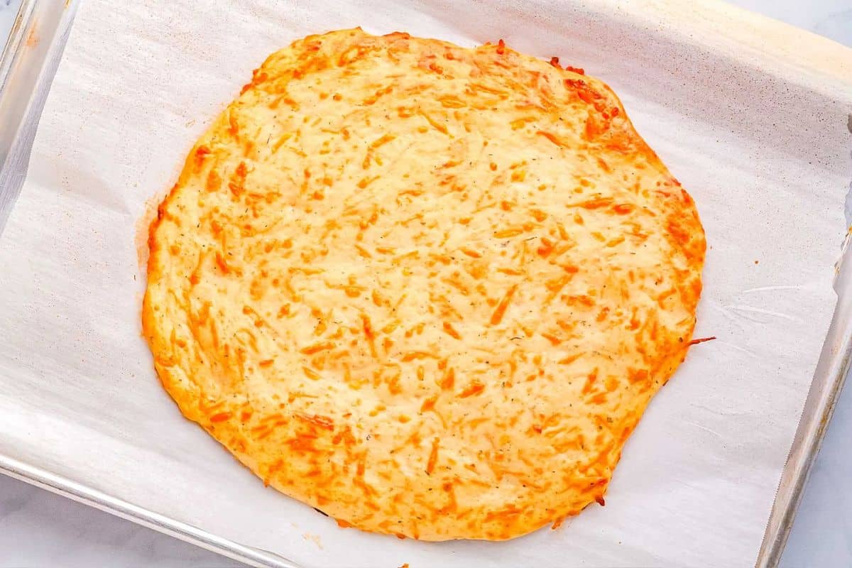 A baked, round, cheese-covered flatbread crust on parchment paper on a baking sheet.