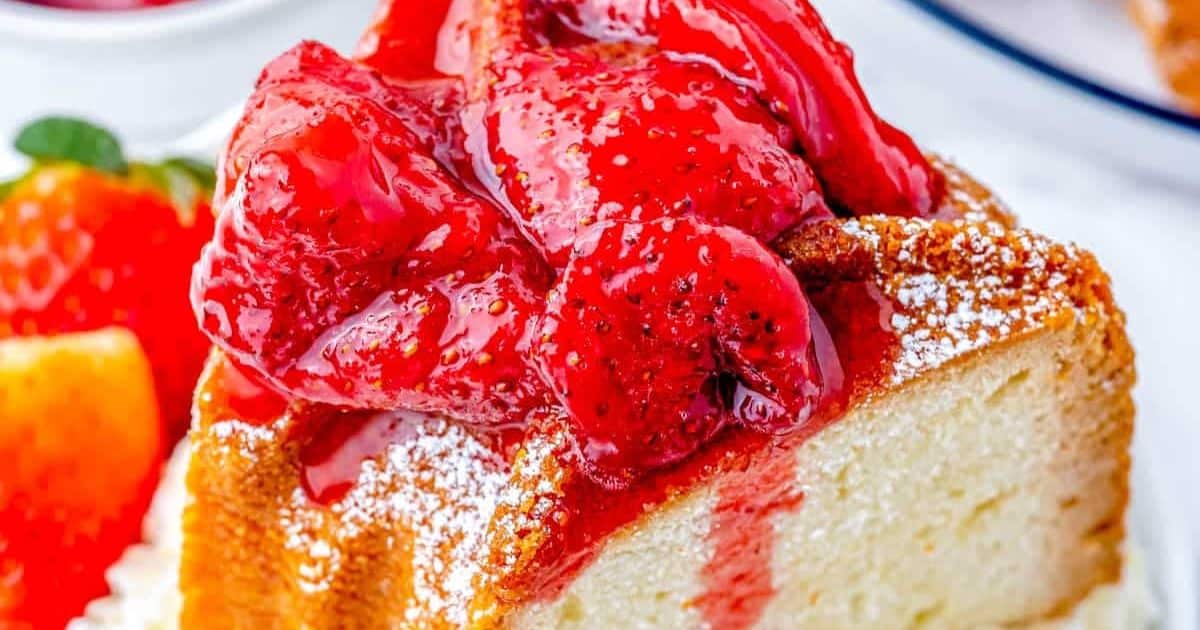 A slice of pound cake topped with glossy strawberry compote and a dusting of powdered sugar.