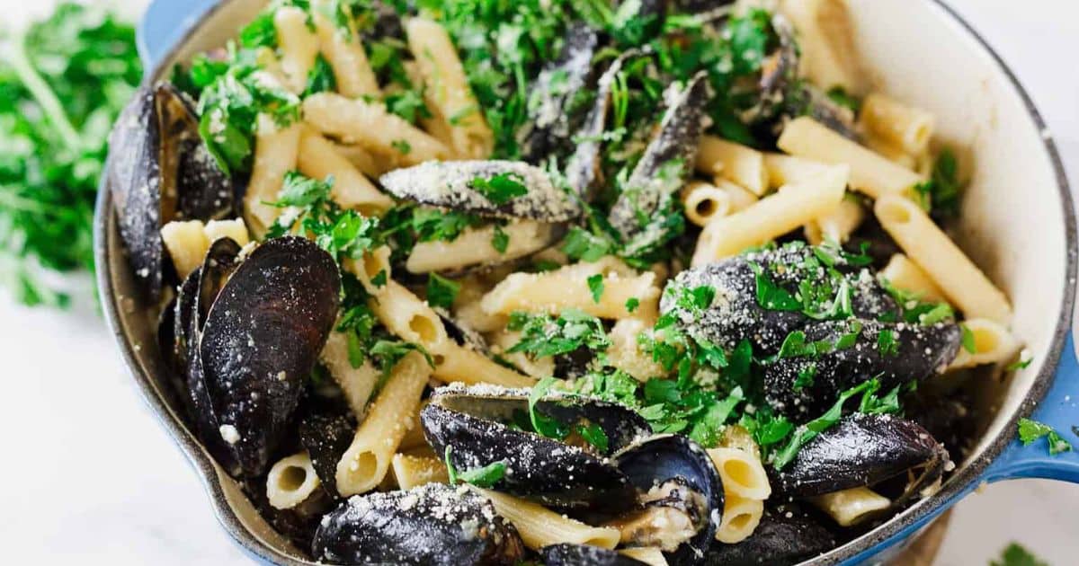 Pasta with mussels, sprinkled with chopped parsley and grated cheese in a blue pot.