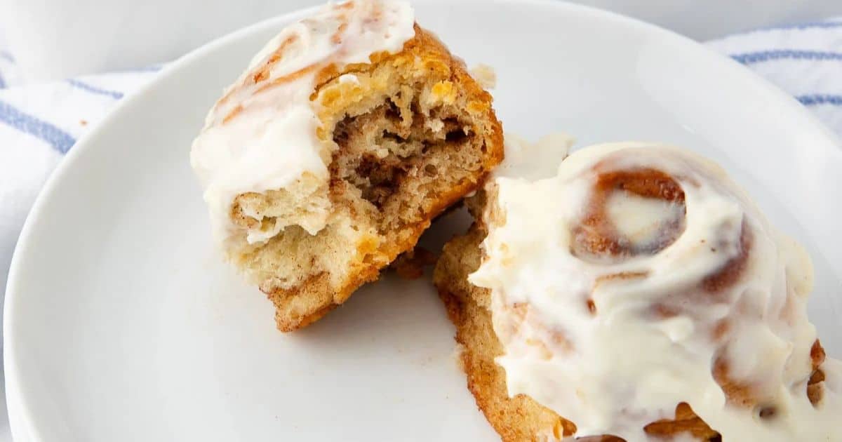 A cinnamon roll with icing, cut in half on a white plate.