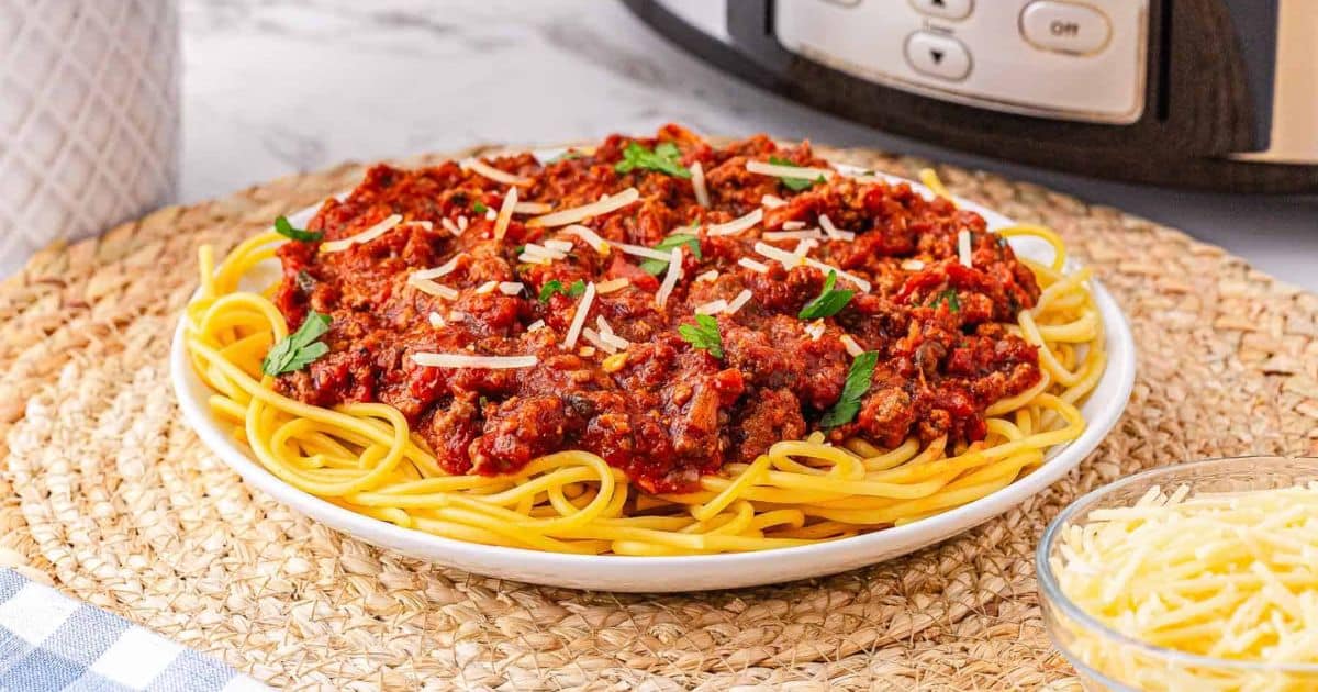 A plate of spaghetti topped with meat sauce, garnished with parsley and shredded cheese, on a woven placemat.