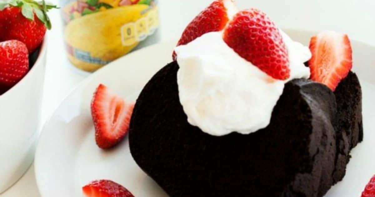 A slice of chocolate cake topped with whipped cream and strawberries on a white plate.