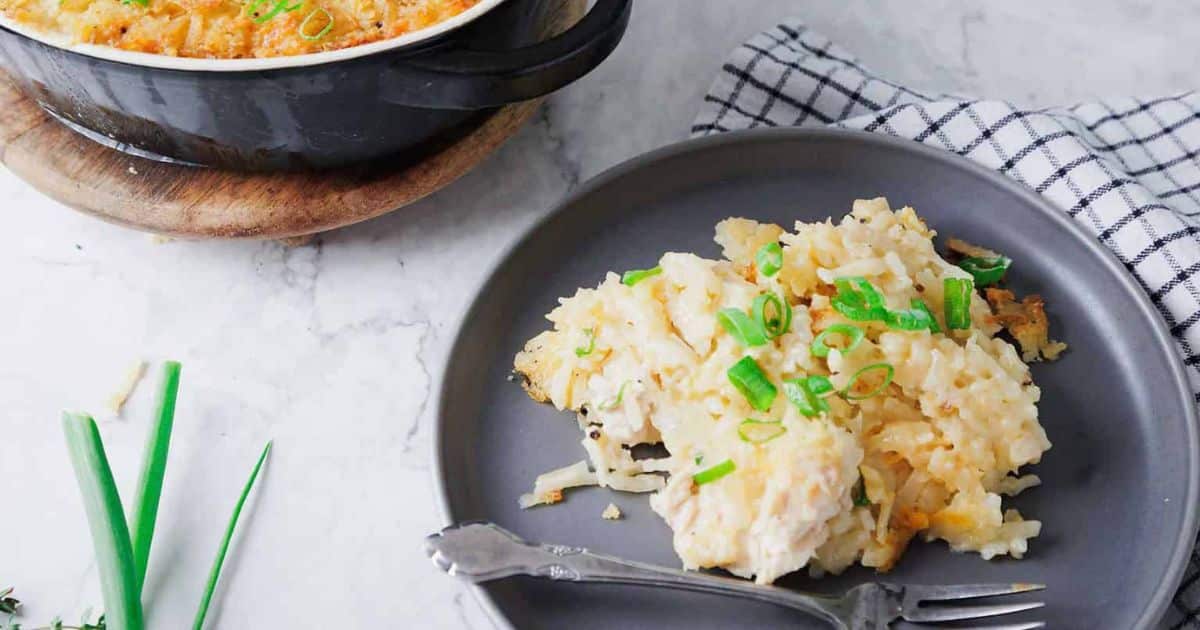 A plate of cheesy chicken and rice casserole topped with chopped green onions, next to a casserole dish.