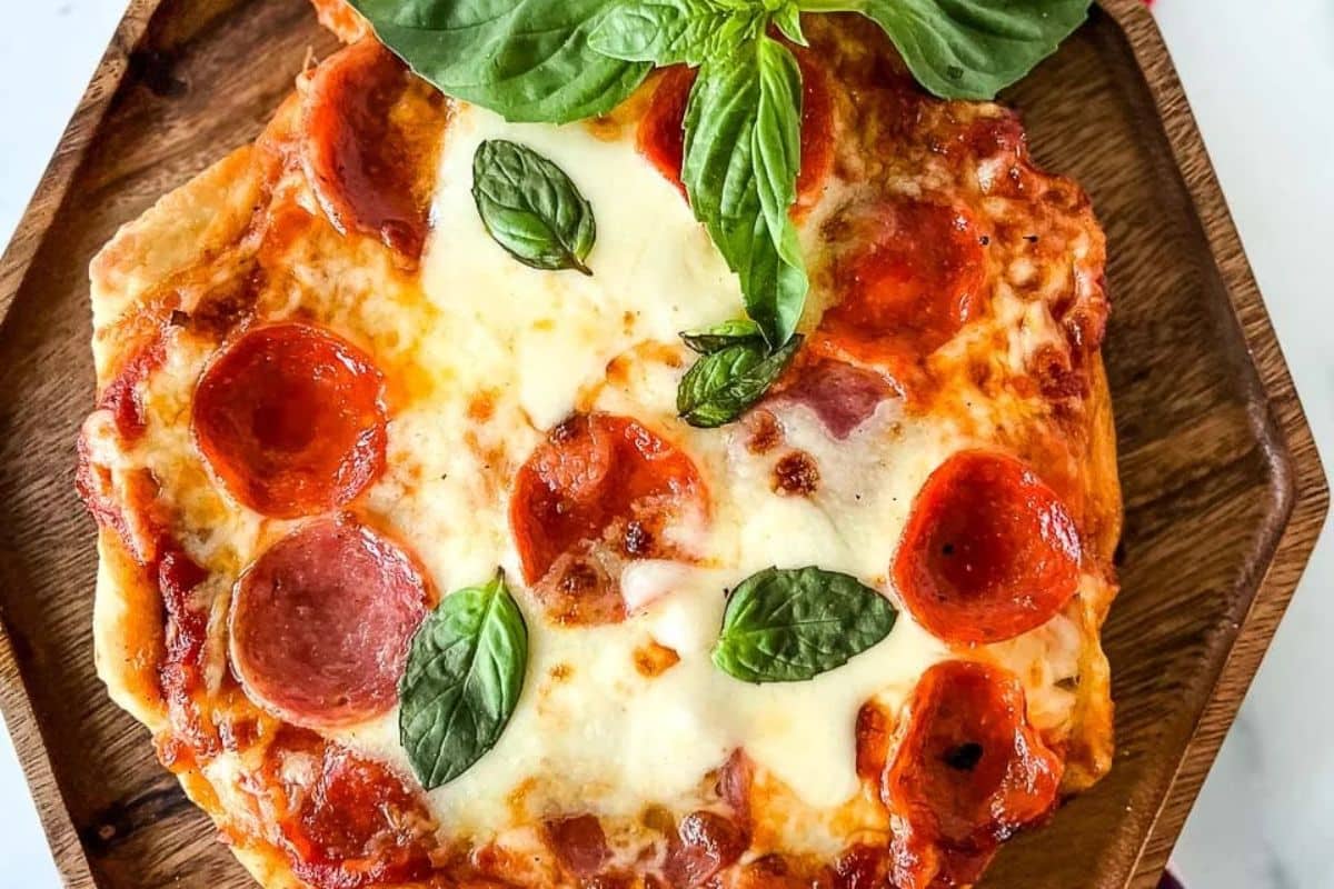 A pepperoni pizza with melted cheese and fresh basil leaves on a wooden plate.
