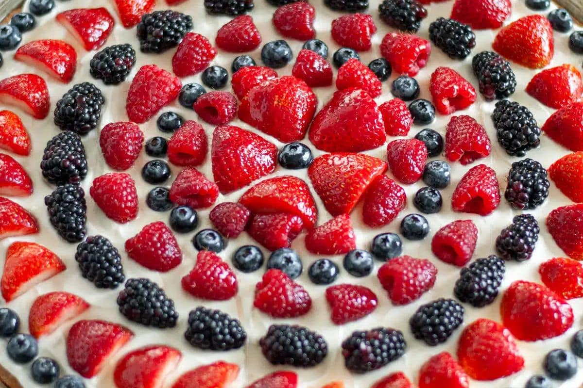 Fresh strawberries, blueberries, and blackberries arranged in circles on a creamy tart base.