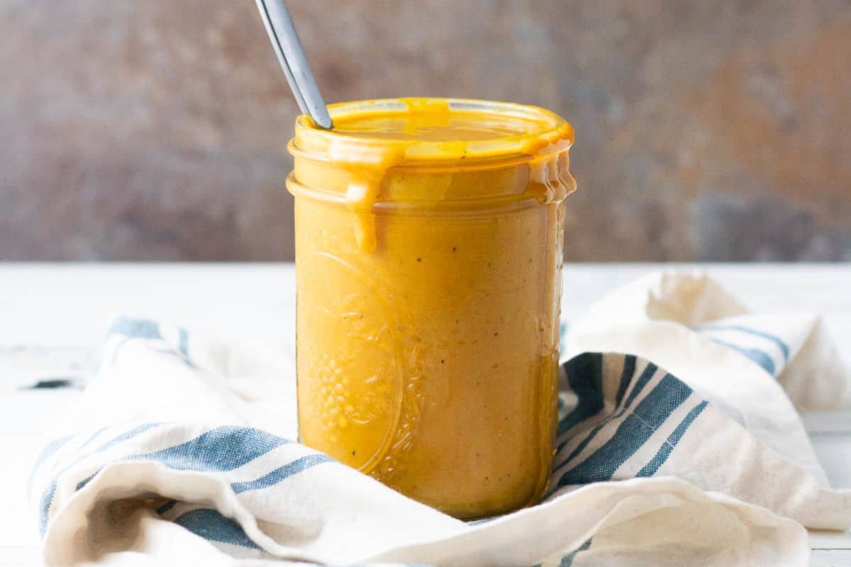 A glass jar of yellow-orange sauce with a spoon inside, sitting on a white towel with blue stripes.