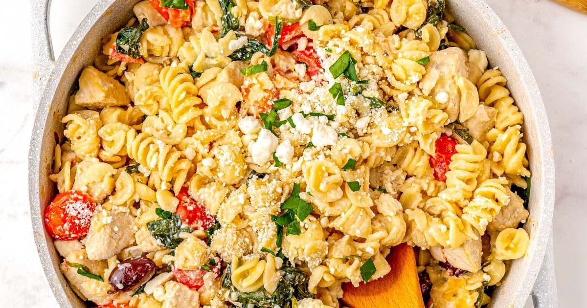 Pasta with chicken, spinach, tomatoes, and cheese in a skillet, topped with herbs and grated cheese.