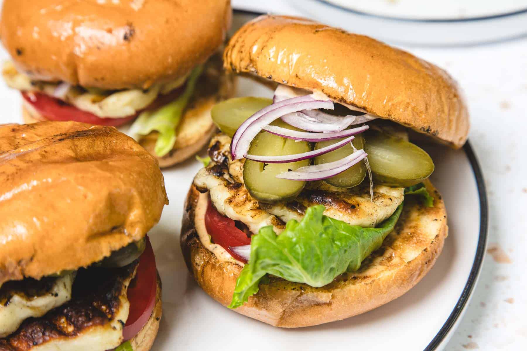 A grilled veggie burger with lettuce, tomato, pickles, and red onion on a toasted bun, served on a plate.