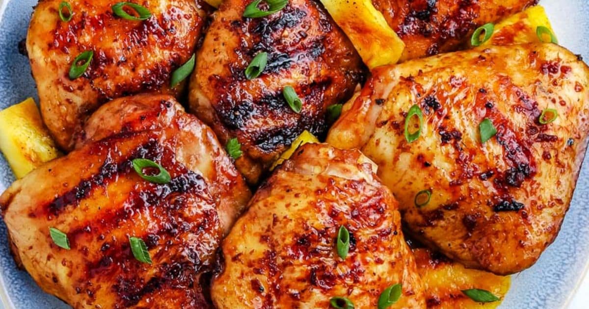 Grilled chicken thighs garnished with green onions, served on a plate with slices of pineapple.
