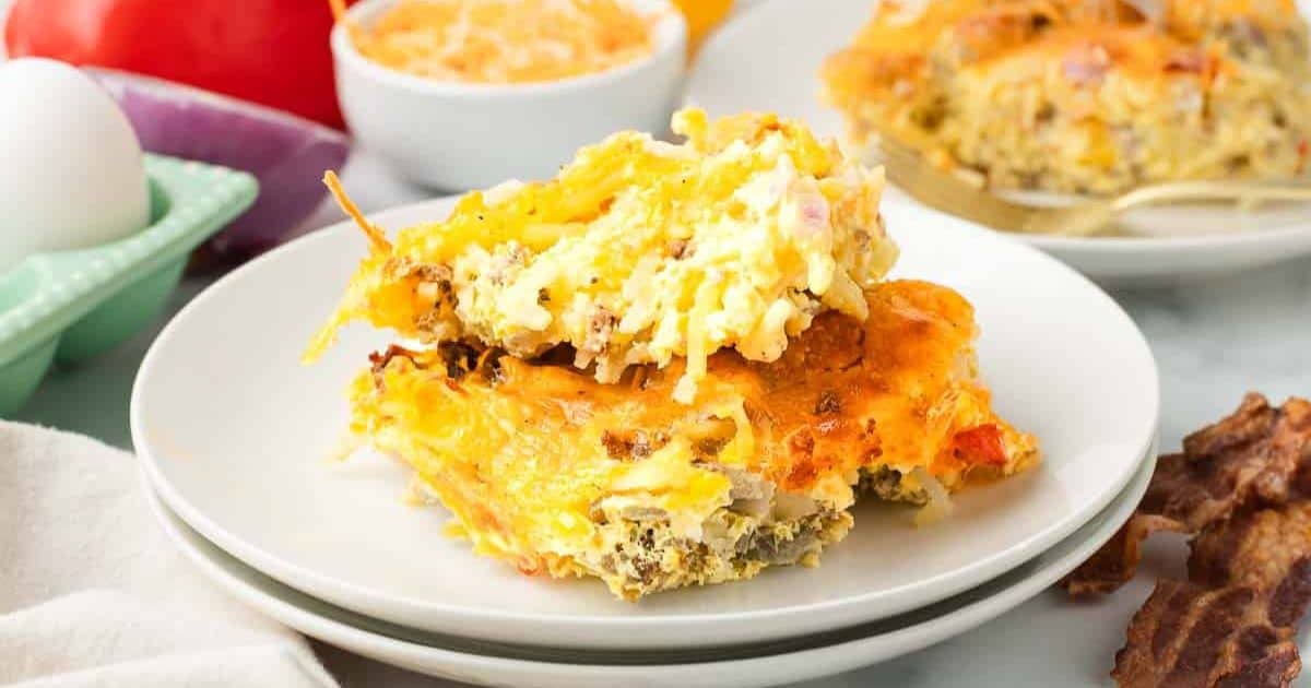 A serving of cheesy breakfast casserole with eggs, sausage, and vegetables on a white plate.