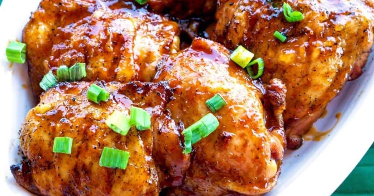 Glazed baked chicken thighs garnished with chopped green onions on a white plate.