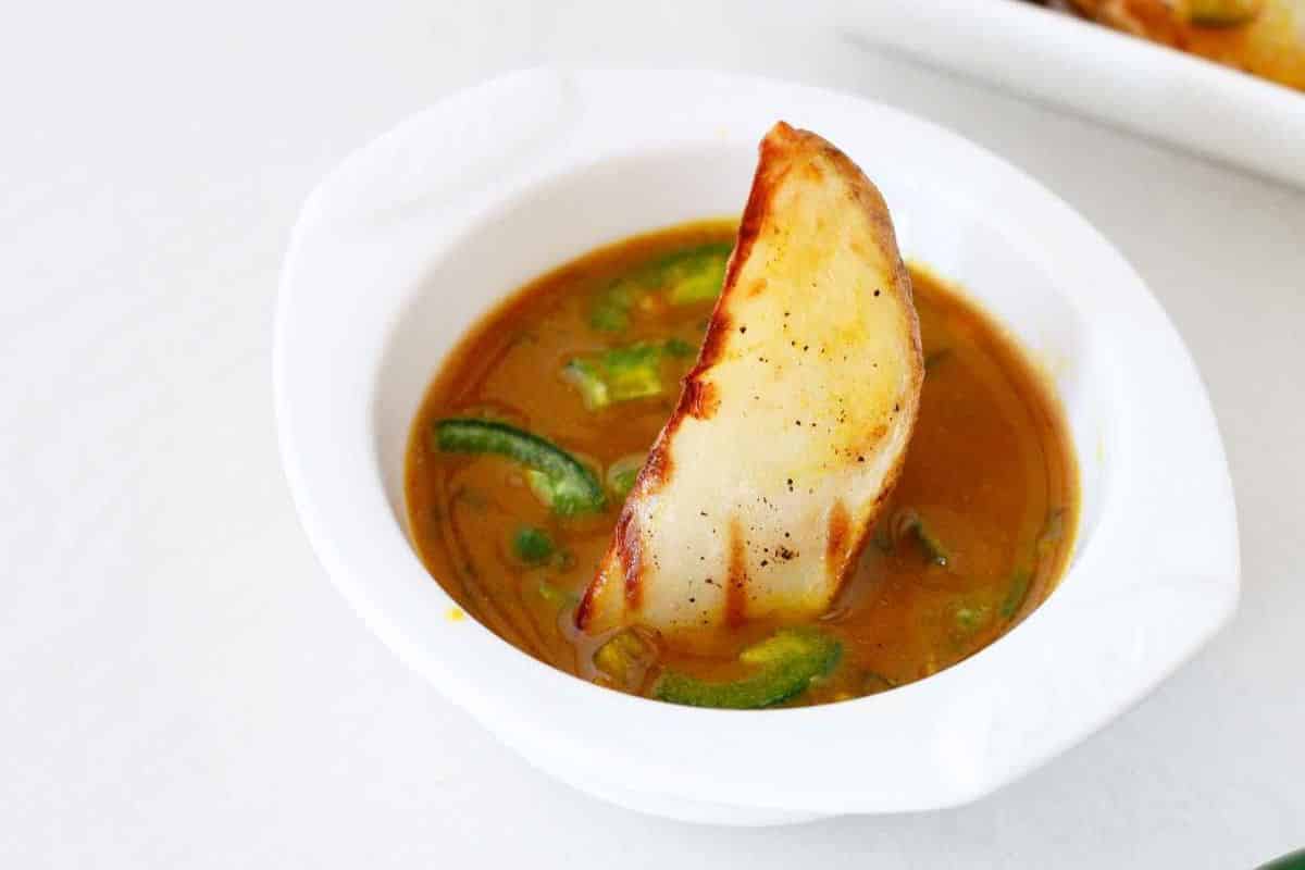 A white bowl of soup with green vegetables and a toasted bread slice on top.