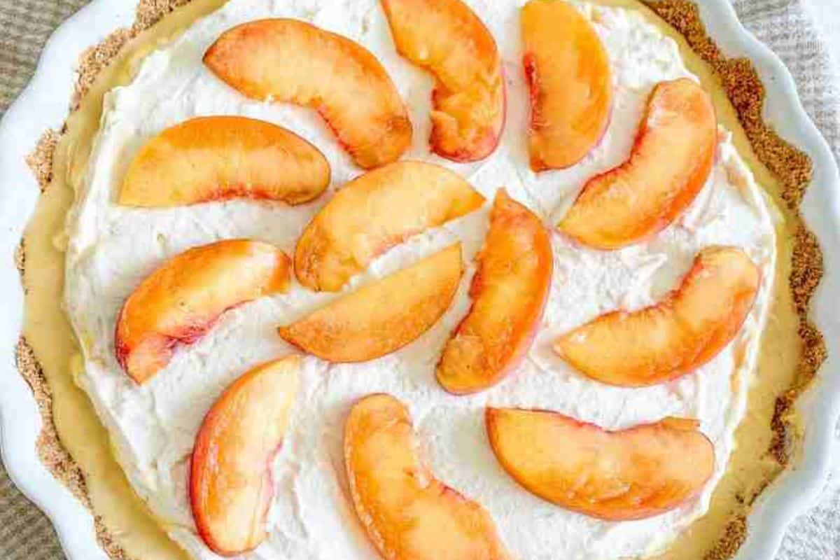 A pie topped with whipped cream and arranged slices of fresh peaches in a white dish.