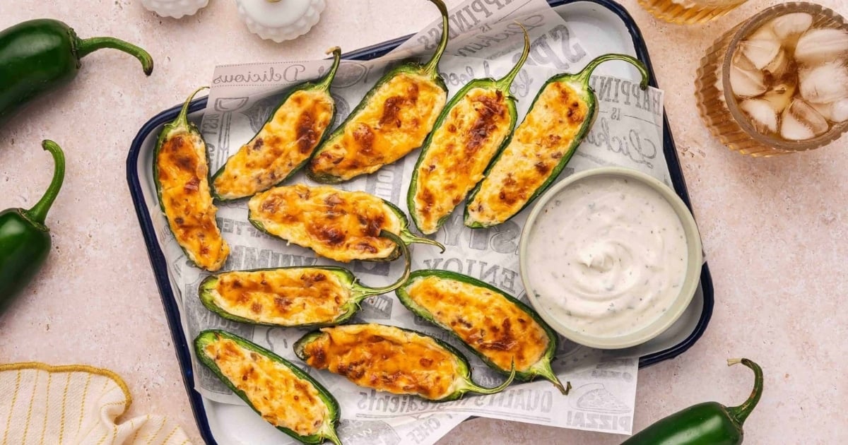 Baked jalapeño poppers with cheesy filling on a tray, served with a bowl of ranch dipping sauce.