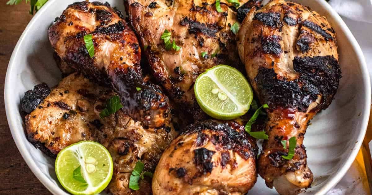 Grilled chicken drumsticks in a bowl, garnished with fresh lime slices and chopped herbs.