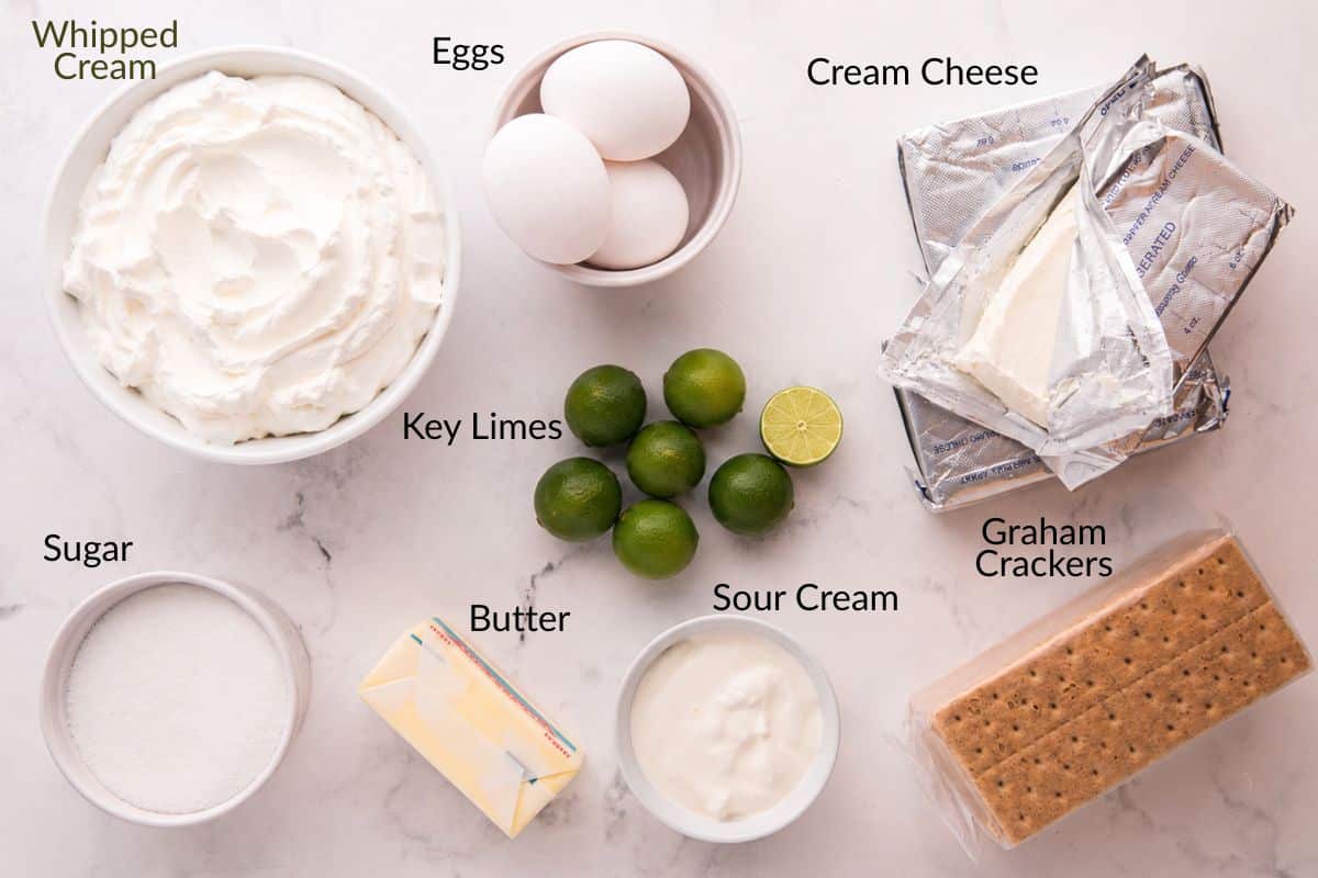 Ingredients for key lime cheesecake: whipped cream, eggs, cream cheese, key limes, sugar, butter, sour cream, graham crackers.