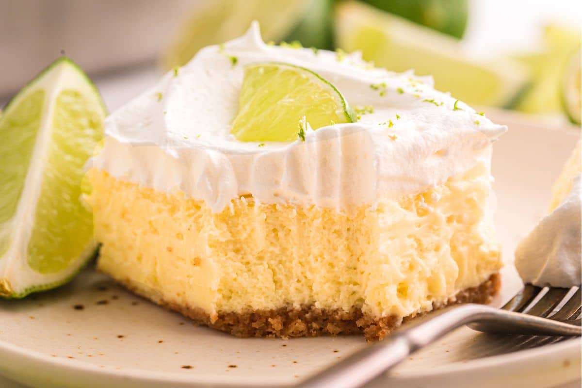 A slice of key lime pie topped with whipped cream and a lime wedge sits on a plate with a fork.