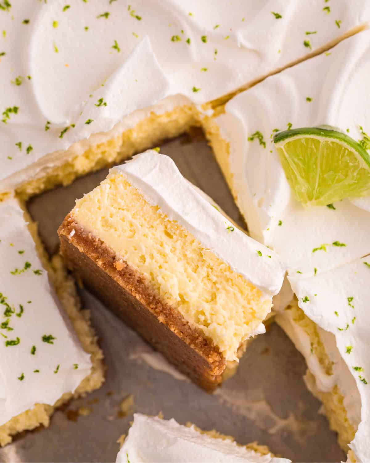 A close-up of creamy, frosted key lime cheesecake bars, one topped with a lime wedge and zest.