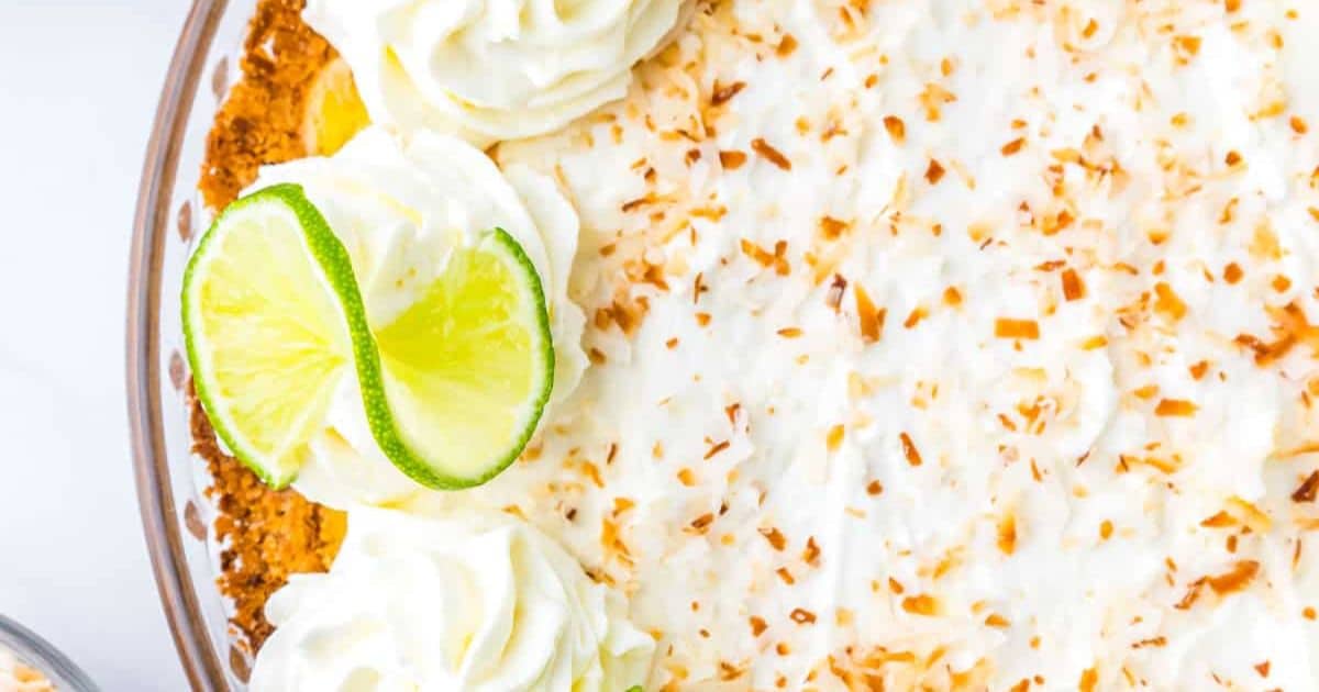 Close-up of a coconut cream pie topped with whipped cream, toasted coconut, and lime slices.