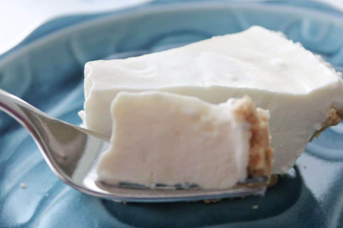 A fork holds a bite of creamy white pie with a crumbly crust on a blue plate.