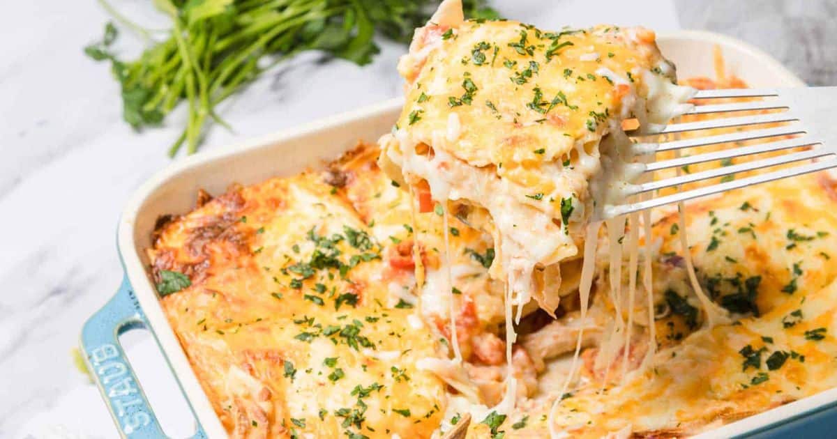 A cheesy baked pasta casserole being served from a dish, topped with melted cheese and herbs.