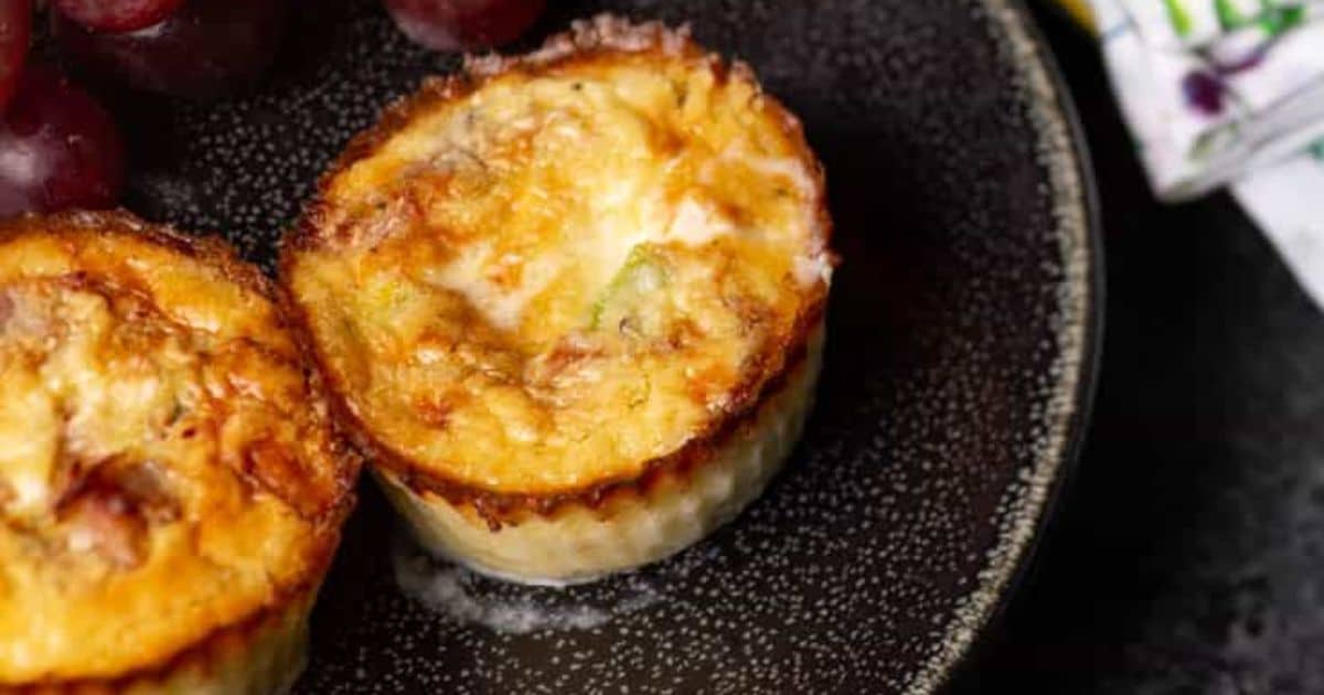 Two mini quiches on a dark plate, served with red grapes, viewed from above.